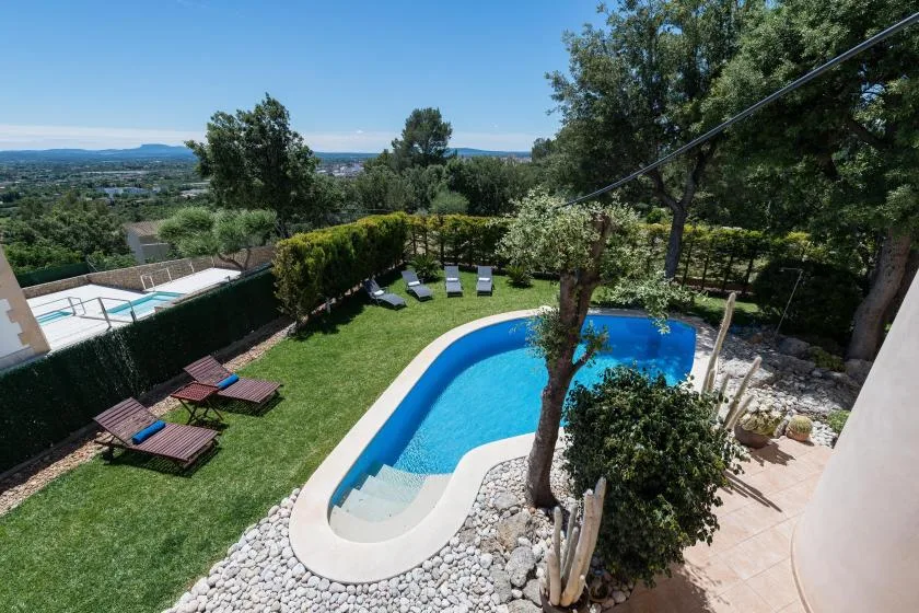 Una piscina en un jardín está rodeada de césped, tumbonas y árboles.