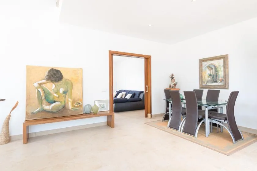Un comedor luminoso con una mesa de vidrio y una puerta abierta hacia una sala de estar.