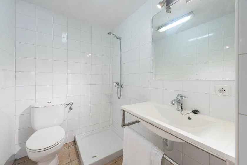 Un baño con azulejos, ducha, inodoro y lavabo bajo un espejo.