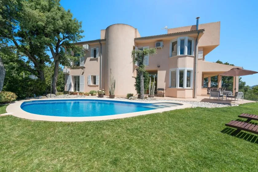 Una casa grande se alza detrás de una piscina y un césped verde.