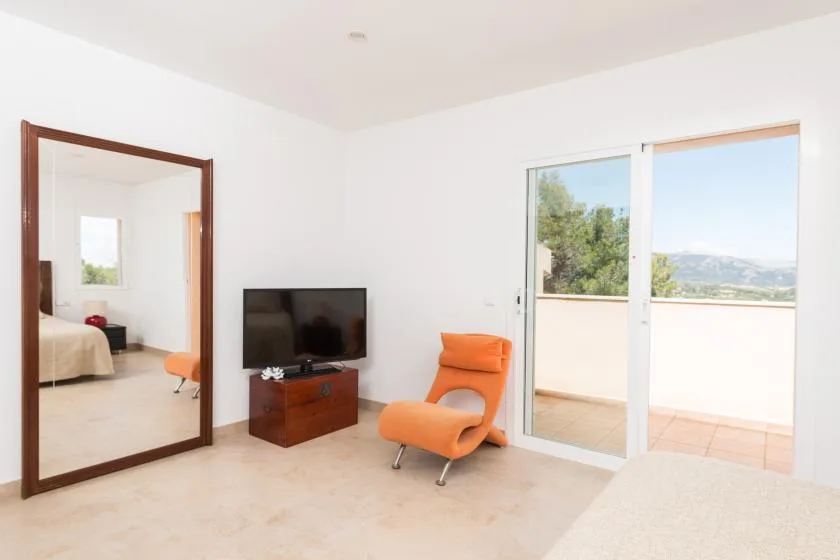 Una sala luminosa con televisor, asientos naranjas y vistas al balcón.