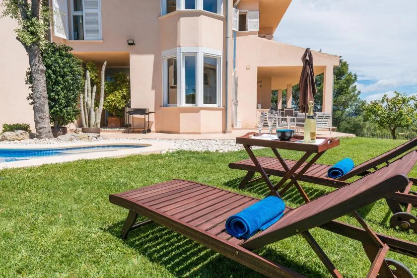 Una casa y una piscina dan a un césped con tumbonas de madera.