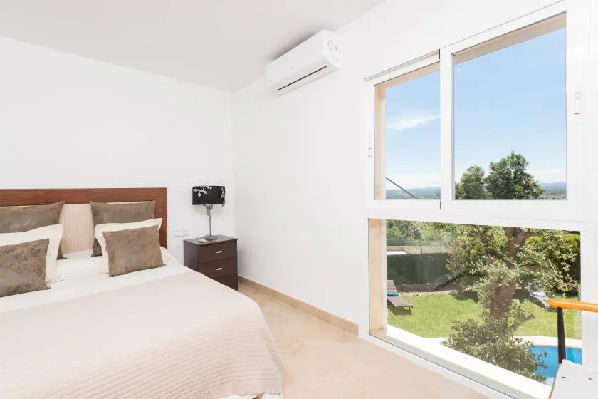 Un dormitorio luminoso con una gran ventana que da a la vegetación y una piscina.