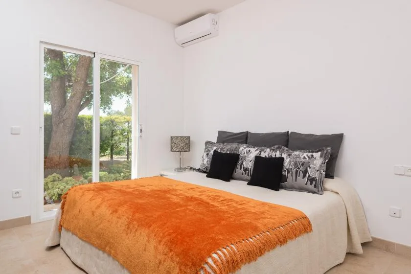 Un dormitorio luminoso con una cama vestida de blanco y una manta naranja.