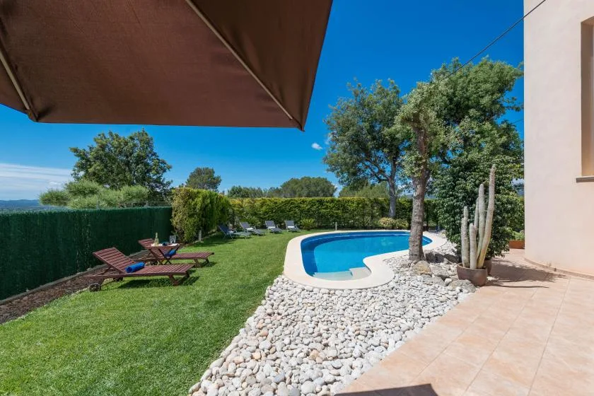 Piscina exterior y jardín con asientos bajo un cielo azul despejado.