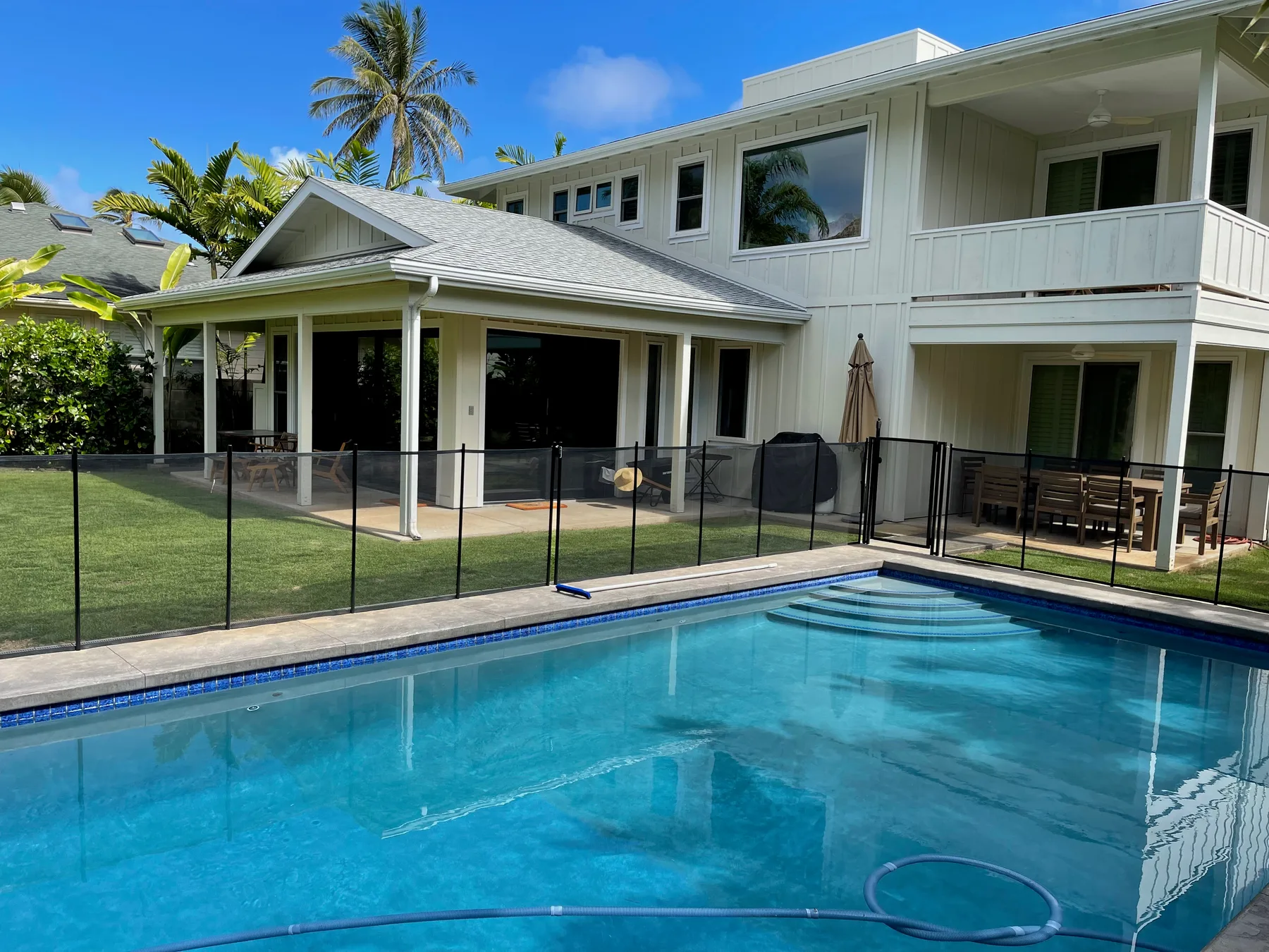 Una piscina está junto a una casa blanca grande y un patio cercado.