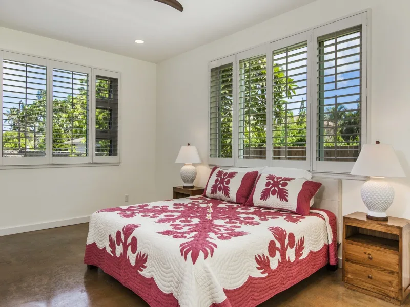 Un dormitorio luminoso con una cama cubierta con una colcha floral roja y blanca.