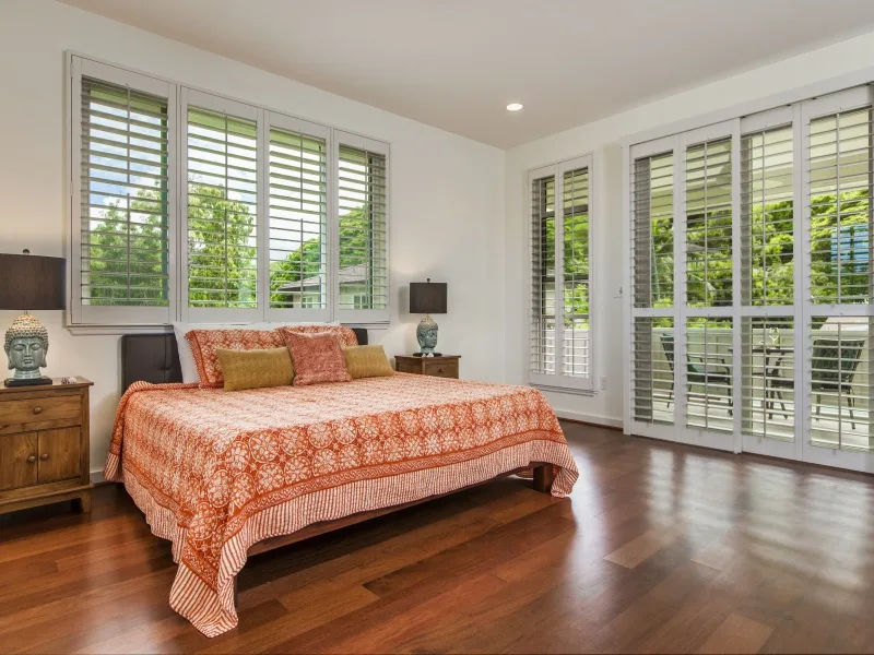 Un dormitorio con una cama bajo ventanas amplias y junto a puertas de vidrio.