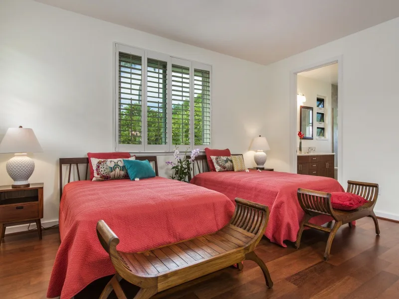 Un dormitorio con dos camas cubiertas de rojo, junto a una ventana y asientos de madera.