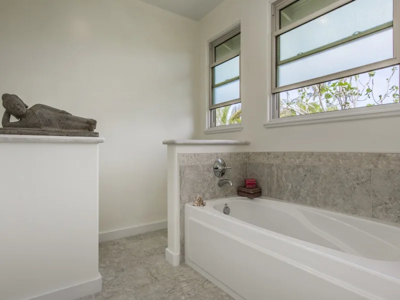 Un baño con una bañera debajo de dos ventanas.