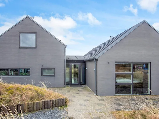 A modern house with gray exterior walls and a paved path leading to its entrance.