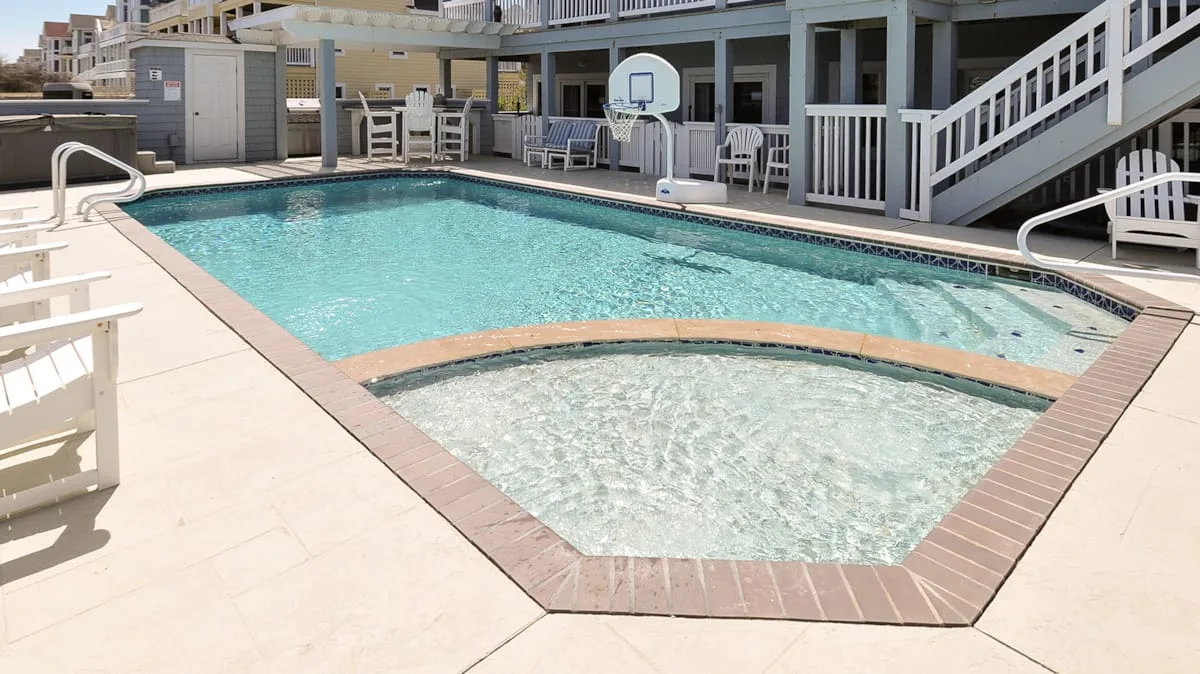 Una piscina y una zona poco profunda están junto a una terraza con barandillas blancas.