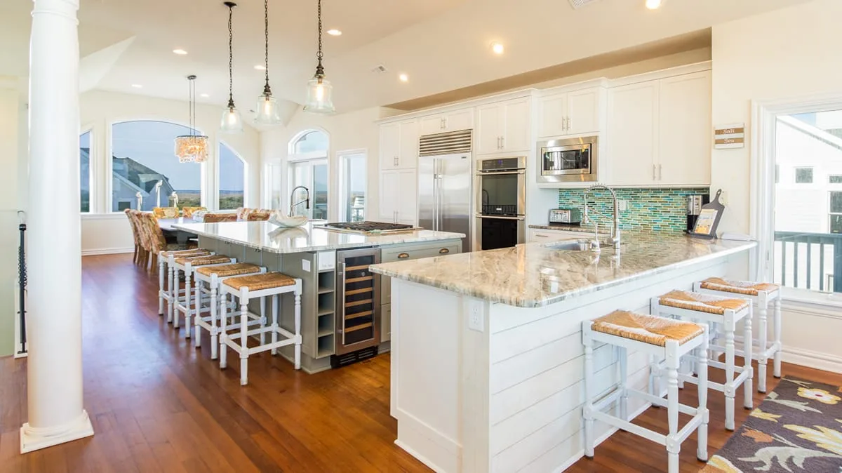 A bright kitchen with white cabinetry, stone counters, and a long island with seating.