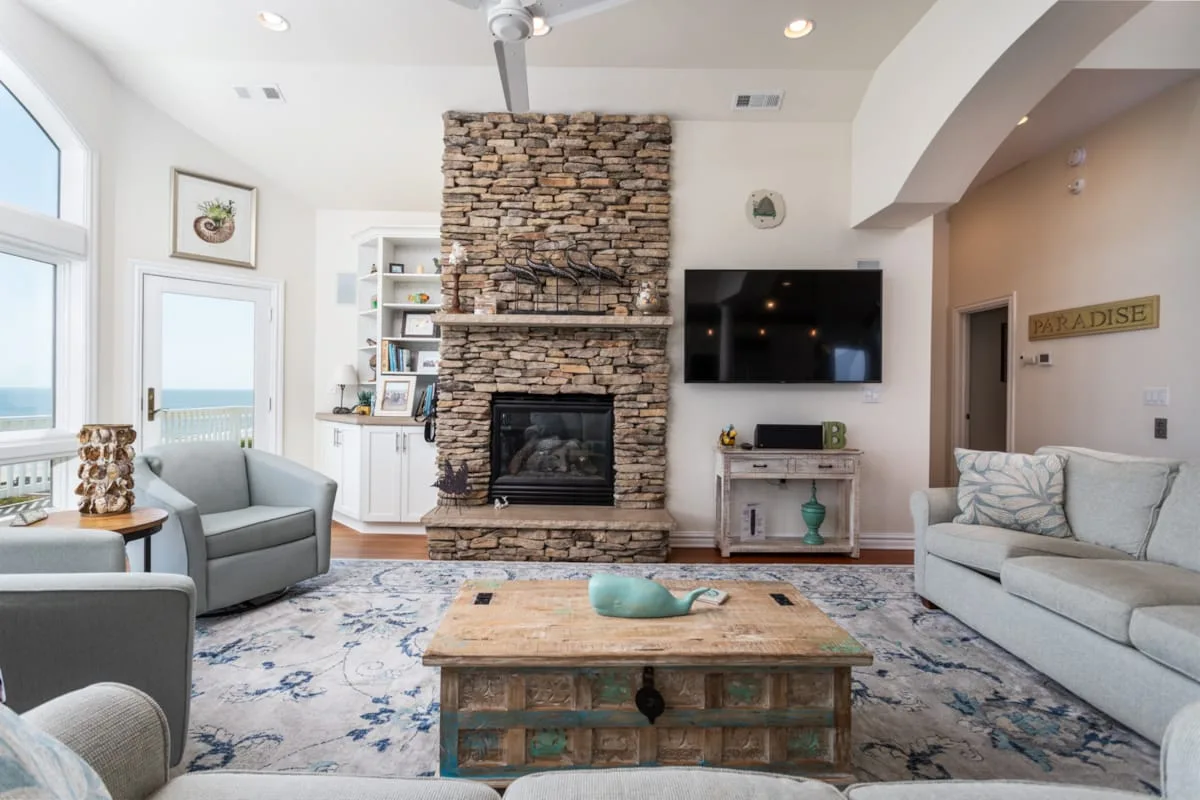 A bright living room with a stone fireplace, seating, and a coffee table.