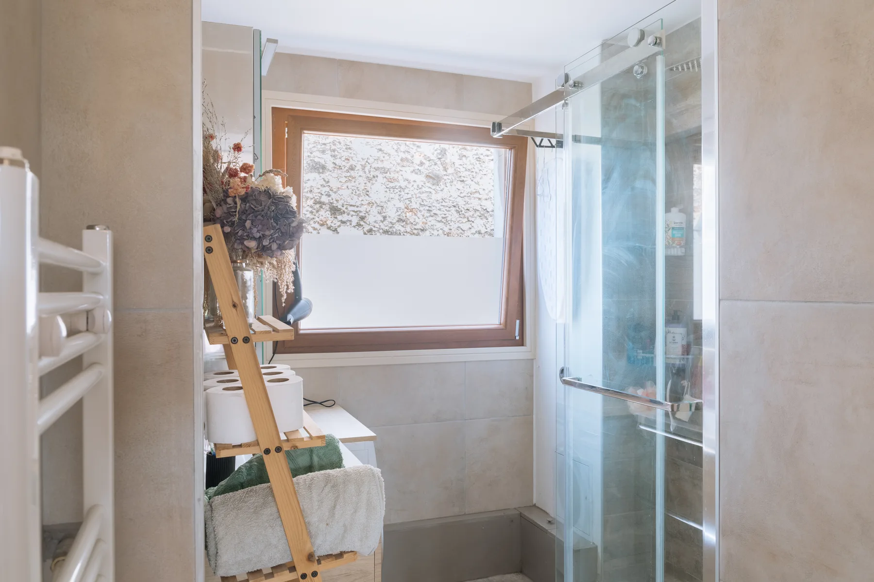 Un baño luminoso con una ducha de vidrio y una ventana.