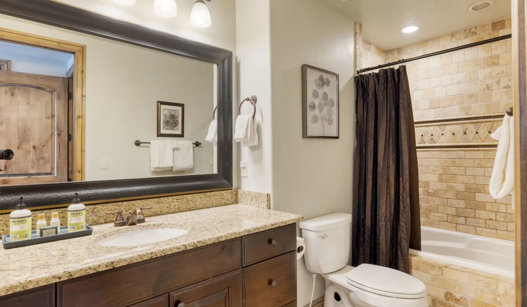A bathroom with a long vanity, mirror, toilet, and bathtub behind a shower curtain.