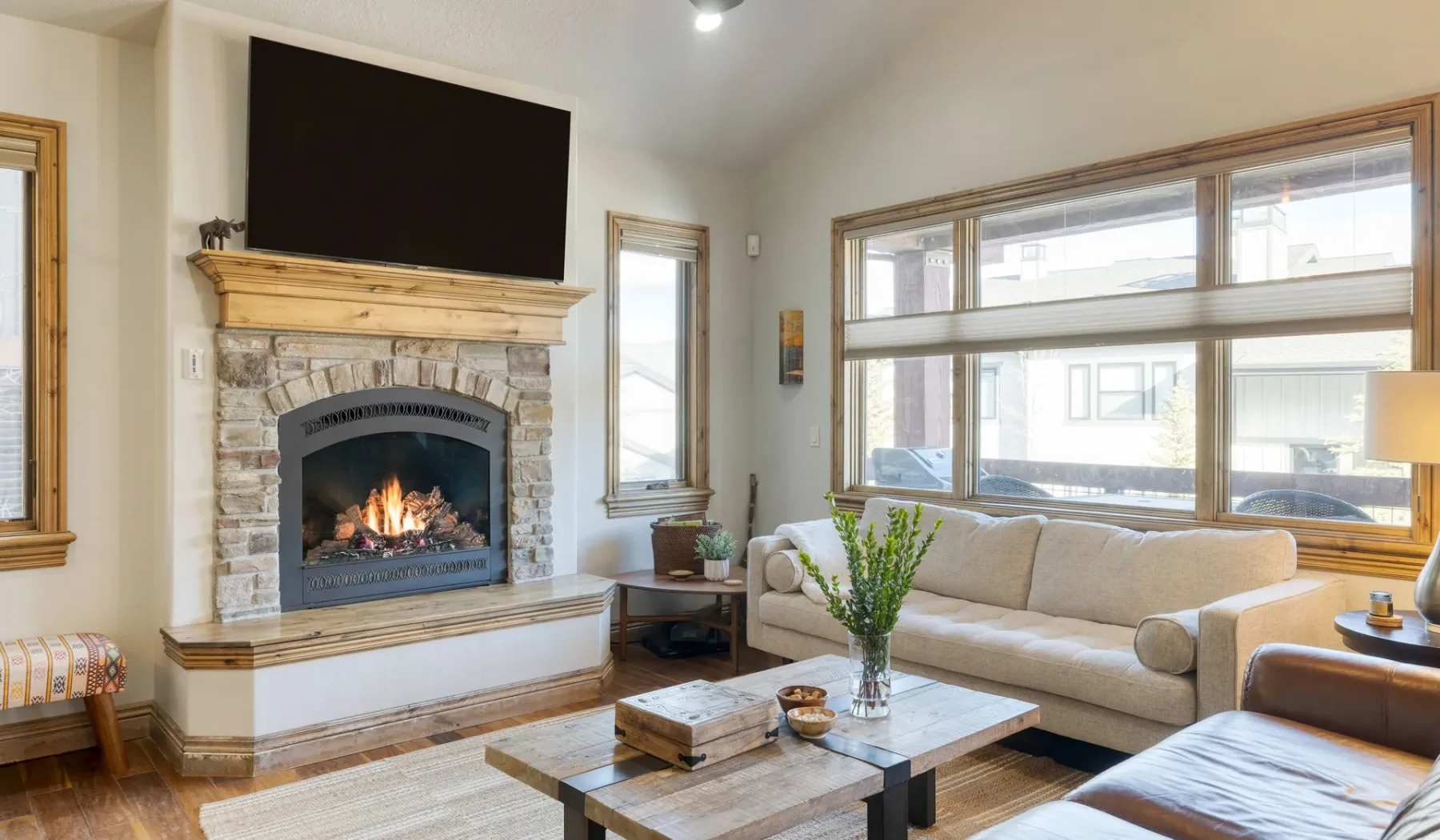 A living room with a stone fireplace and seating beside large windows.