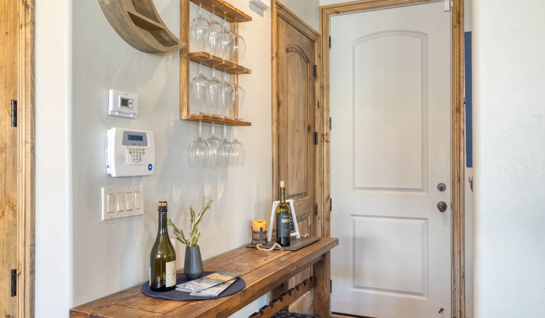 An entryway with a wooden console table, glassware shelves, and a white door.