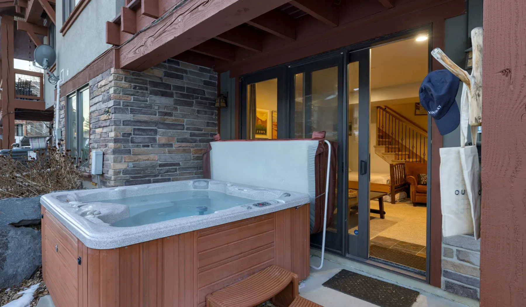 An outdoor hot tub sits beside a glass doorway leading into a warmly lit interior.