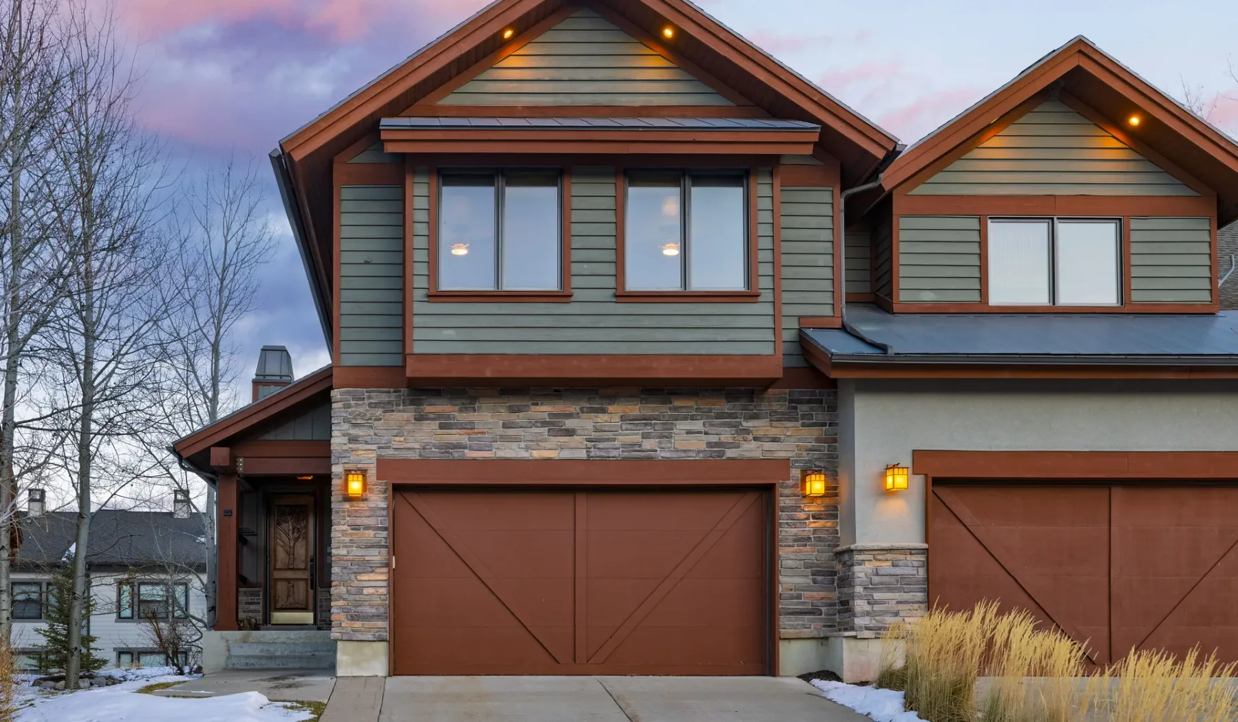 A two-story house with brown garage doors stands beside a snow-covered driveway.