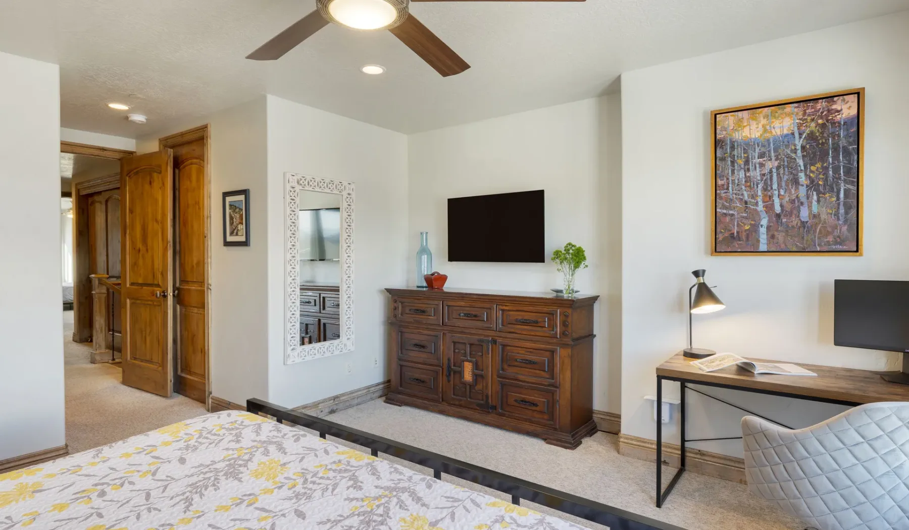 A bedroom with a dark wooden dresser, wall-mounted television, and desk.