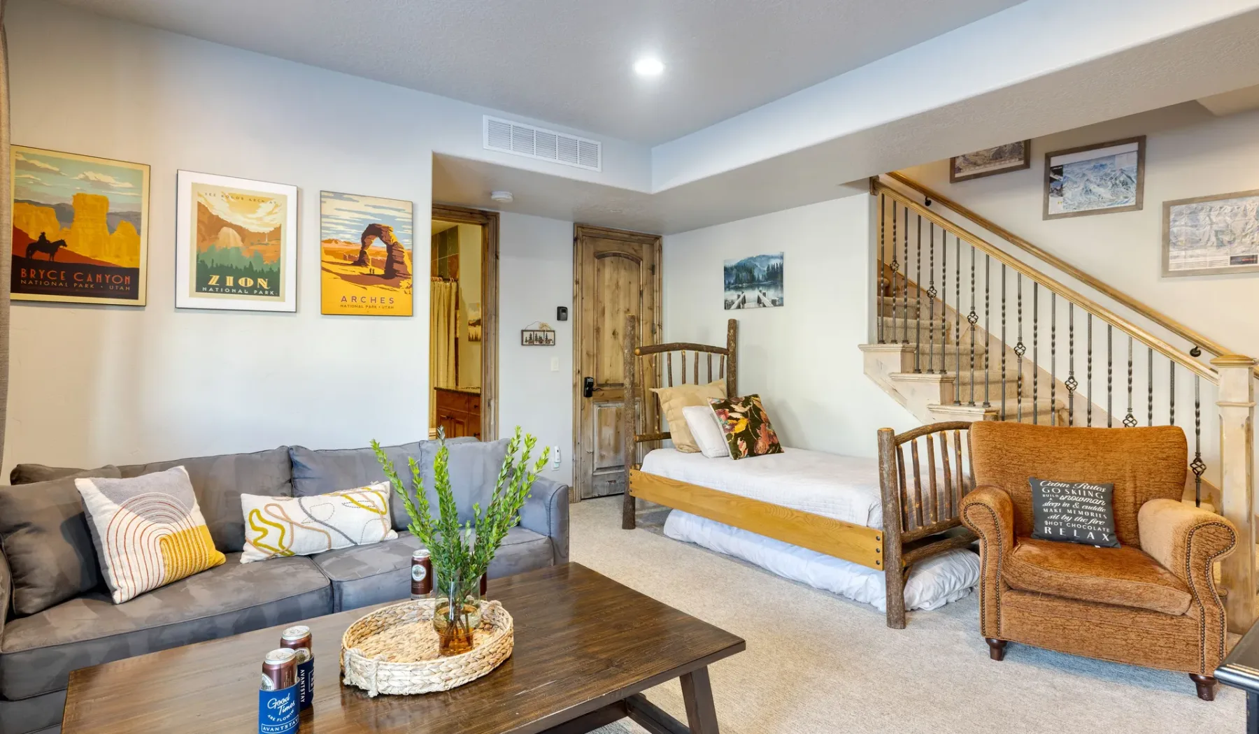 A living room with a sofa, armchair, and a bed beneath the staircase.