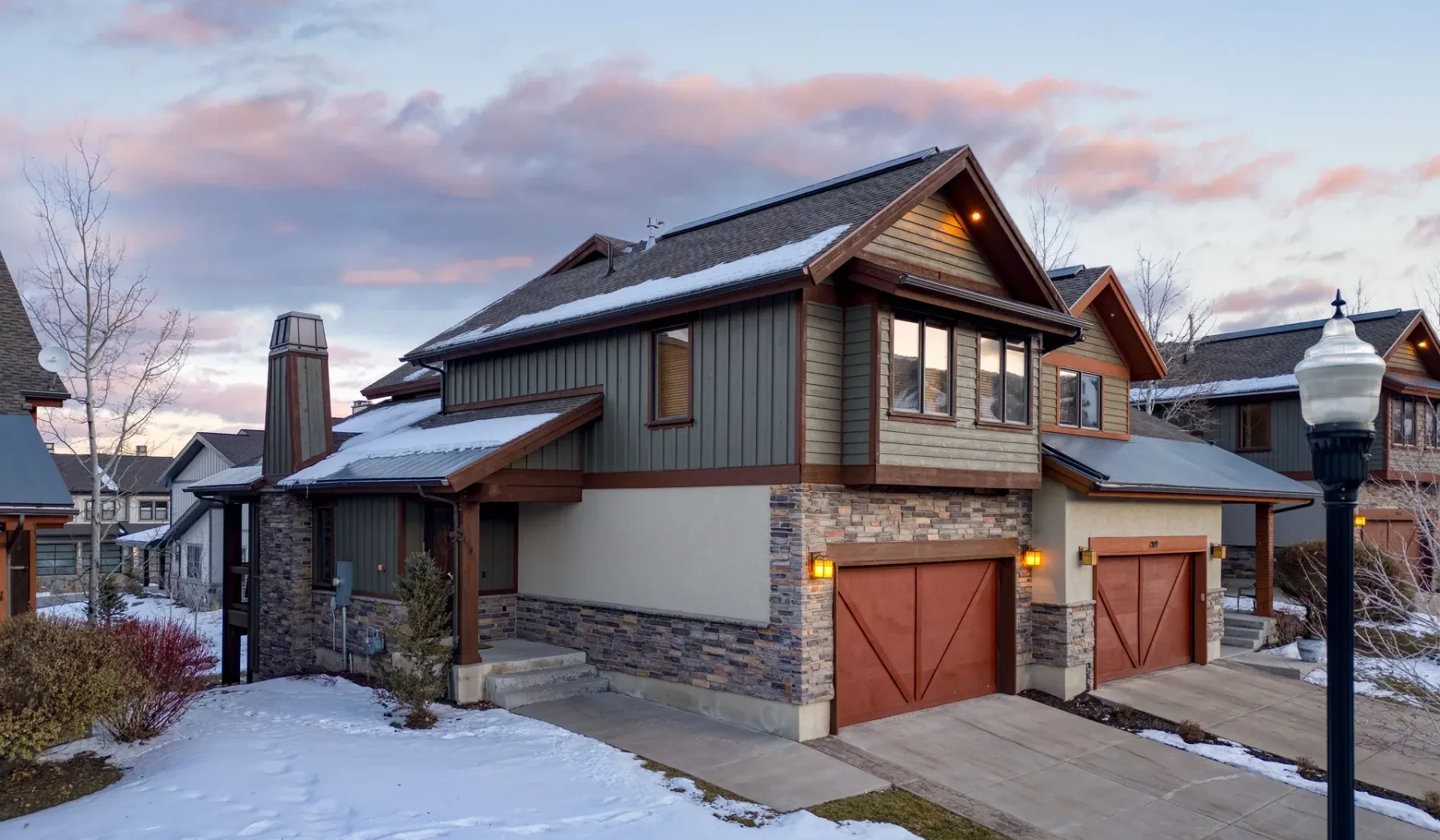 Snow-covered residential buildings stand beside a driveway beneath a colorful evening sky.