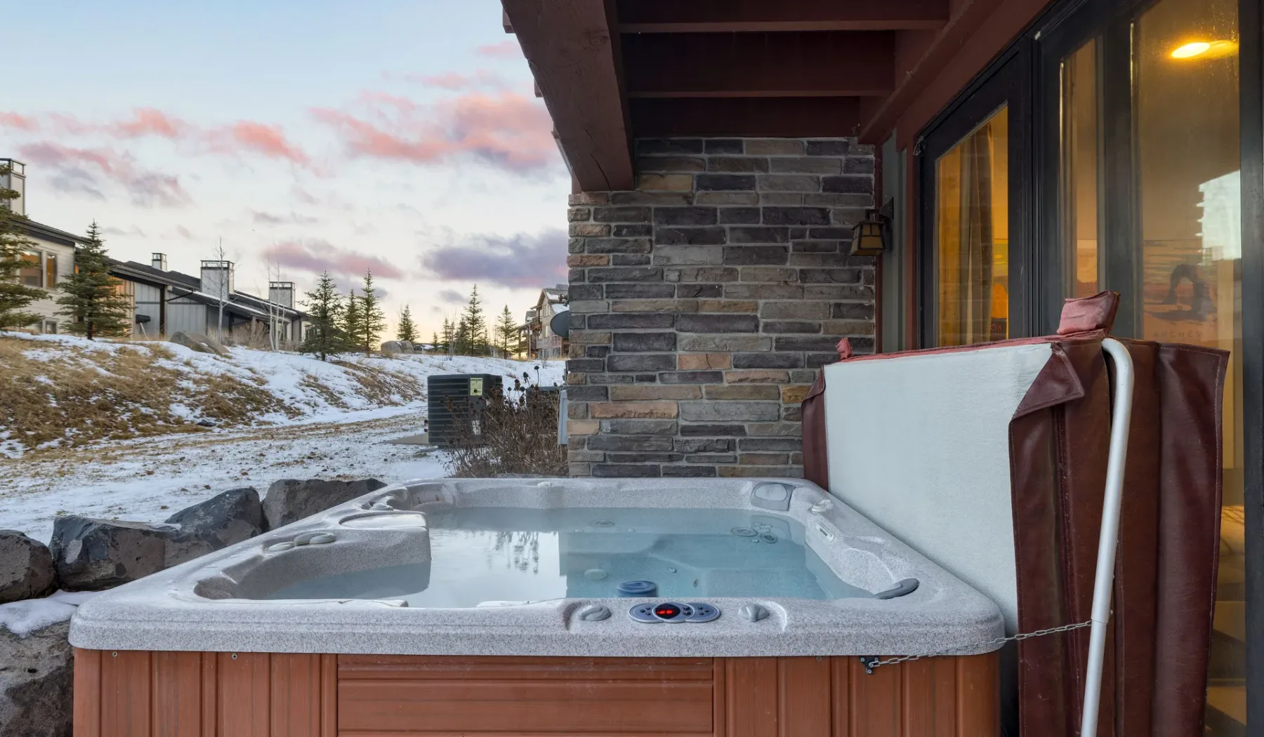 An outdoor hot tub sits beside a stone wall, with a snowy landscape beyond.