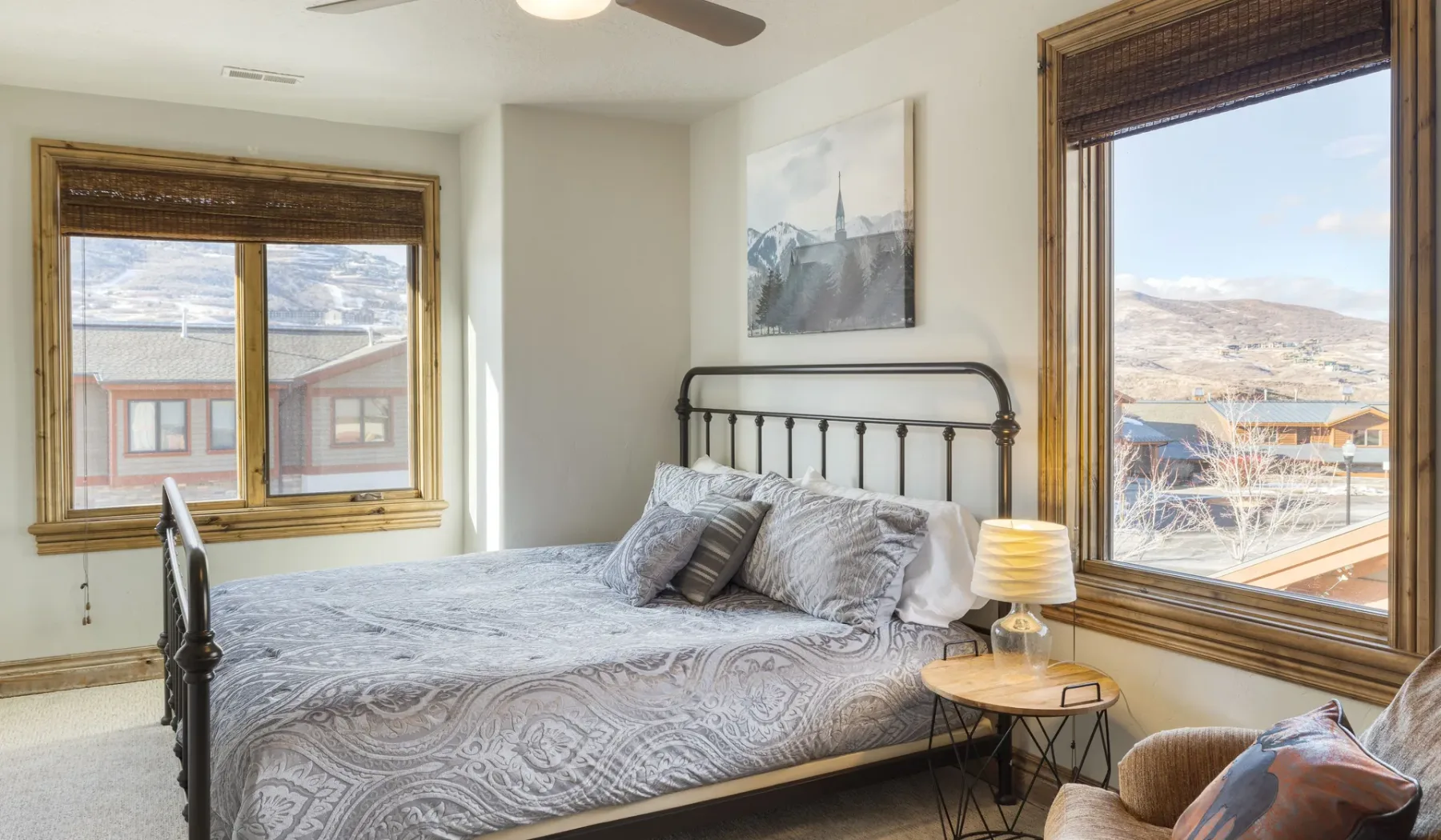 A bedroom with a bed beside two windows overlooking the surrounding landscape.