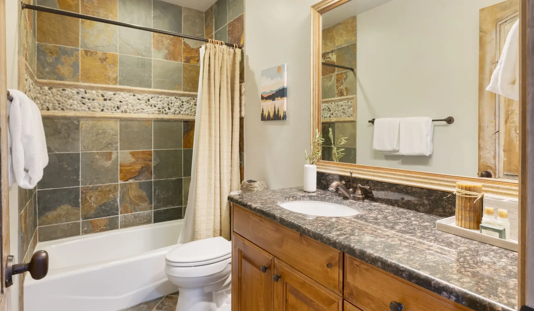 A bathroom with a tiled bathtub and a wood vanity topped by a sink.