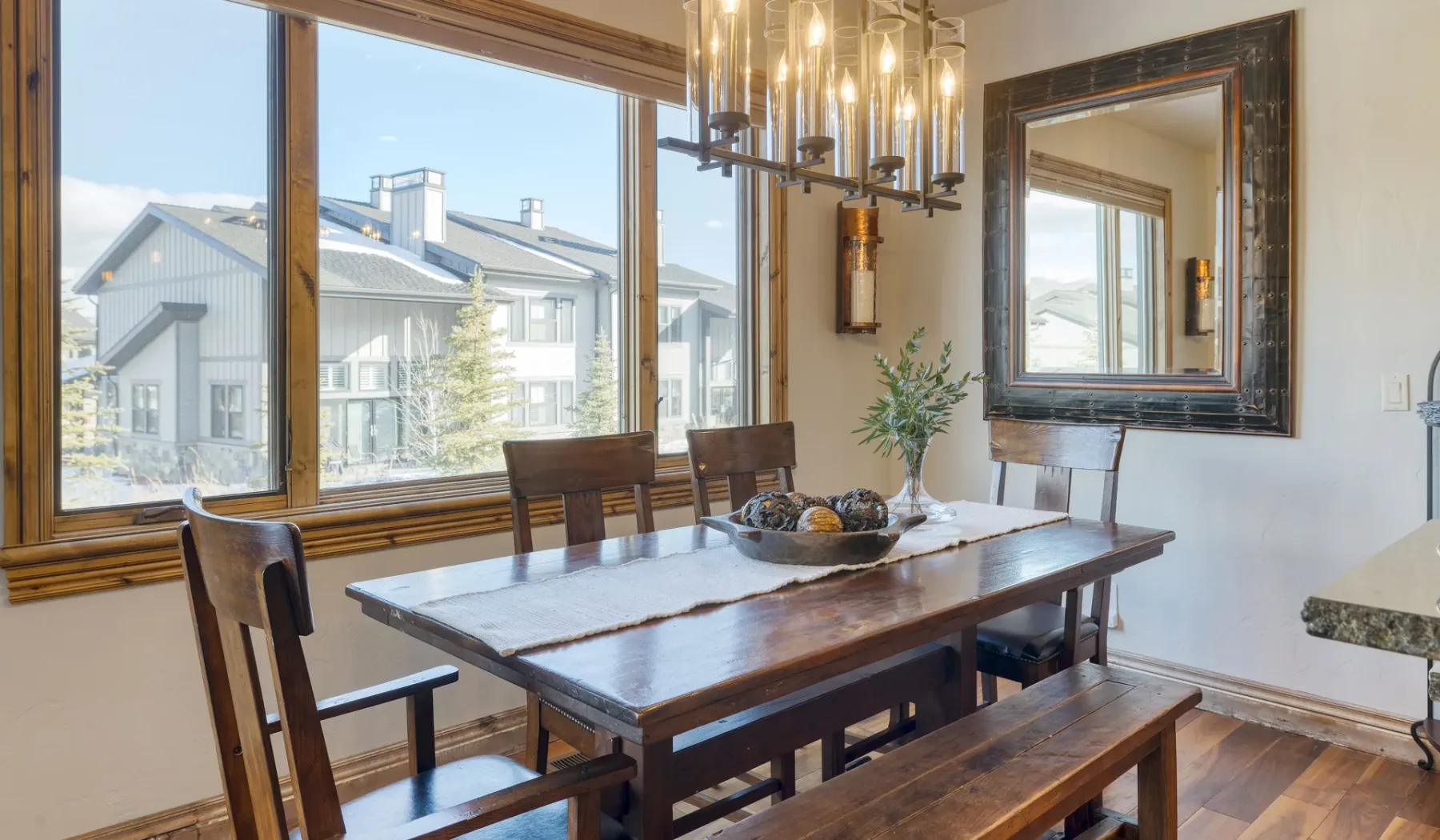 A dining room with a wooden table and large windows overlooking neighboring homes.