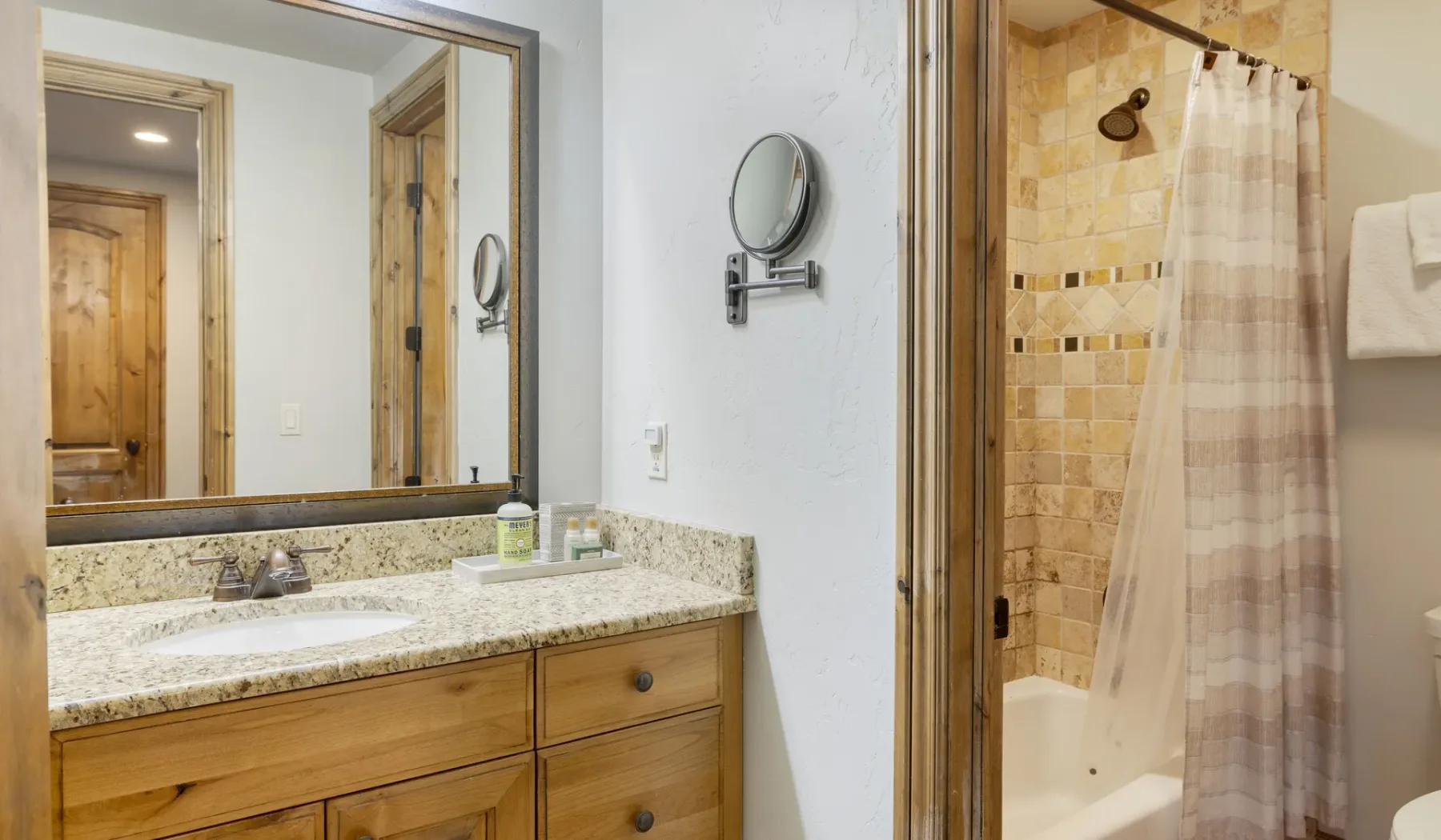 A bathroom vanity and mirror stand beside a shower with a curtain.