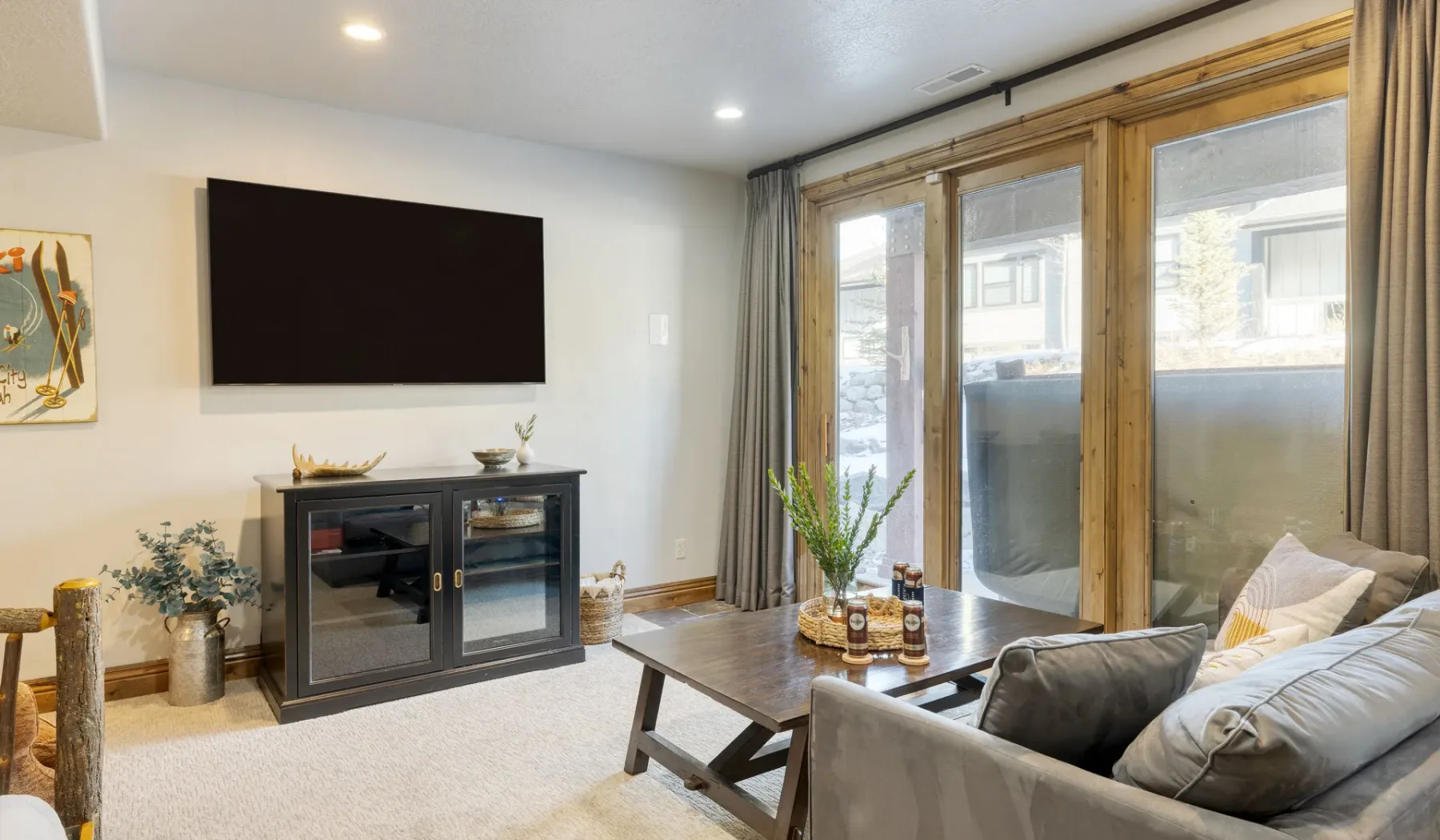 A living room with a television, seating, and large windows.