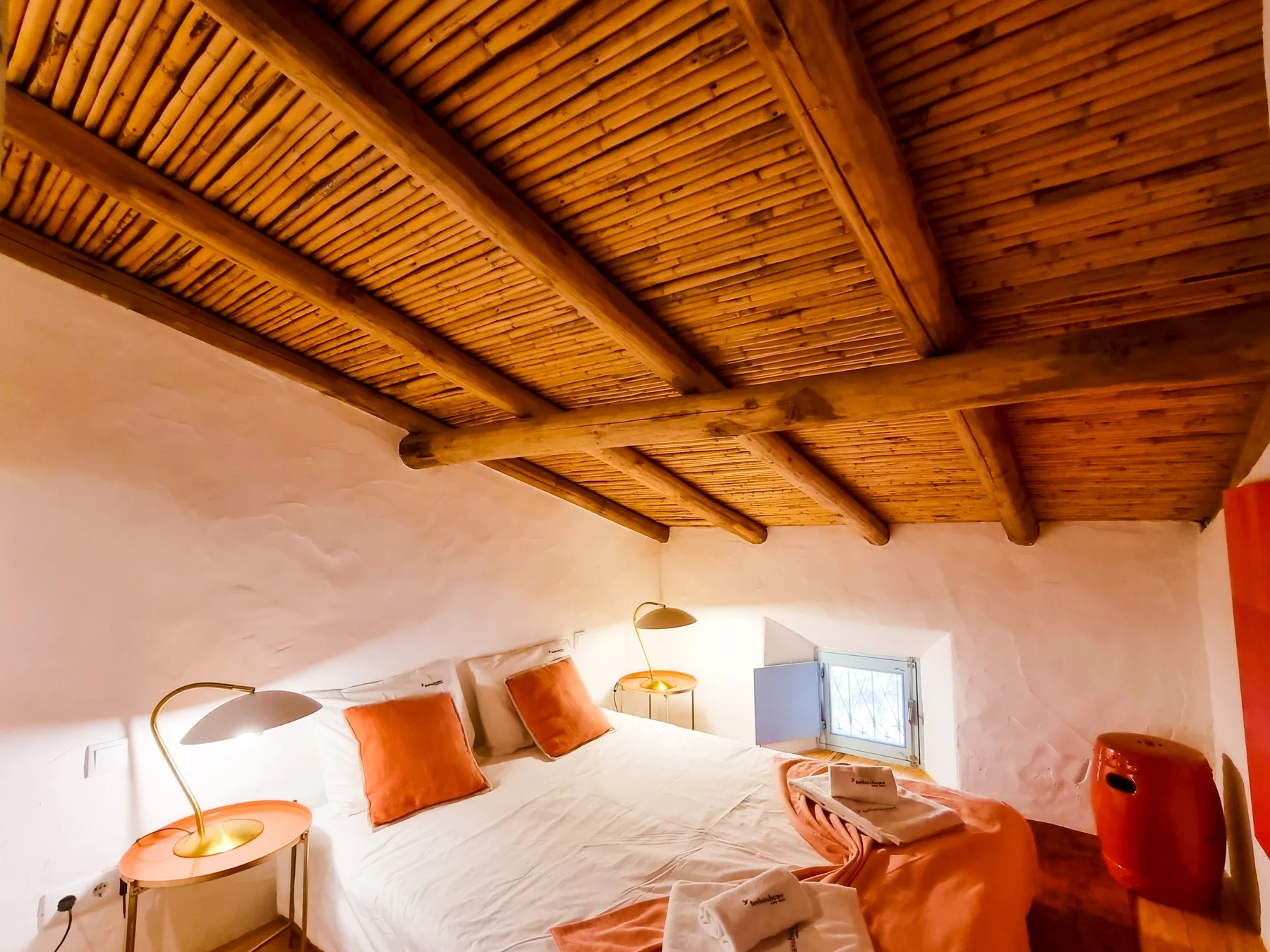Un dormitorio con techo bajo de madera, una cama y lámparas de noche.