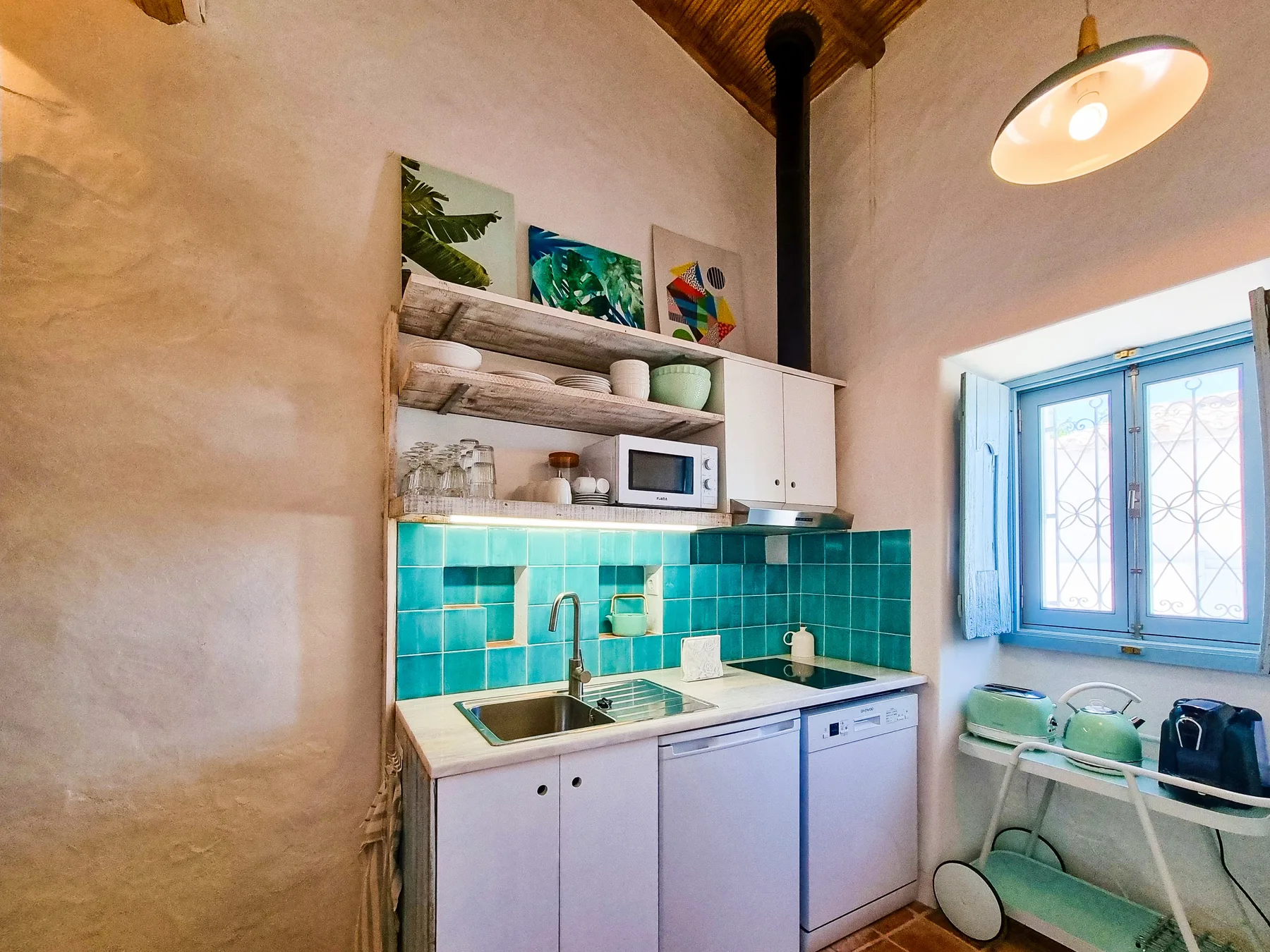 Una pequeña cocina con salpicadero de azulejos turquesa, fregadero y electrodomésticos sobre la encimera.