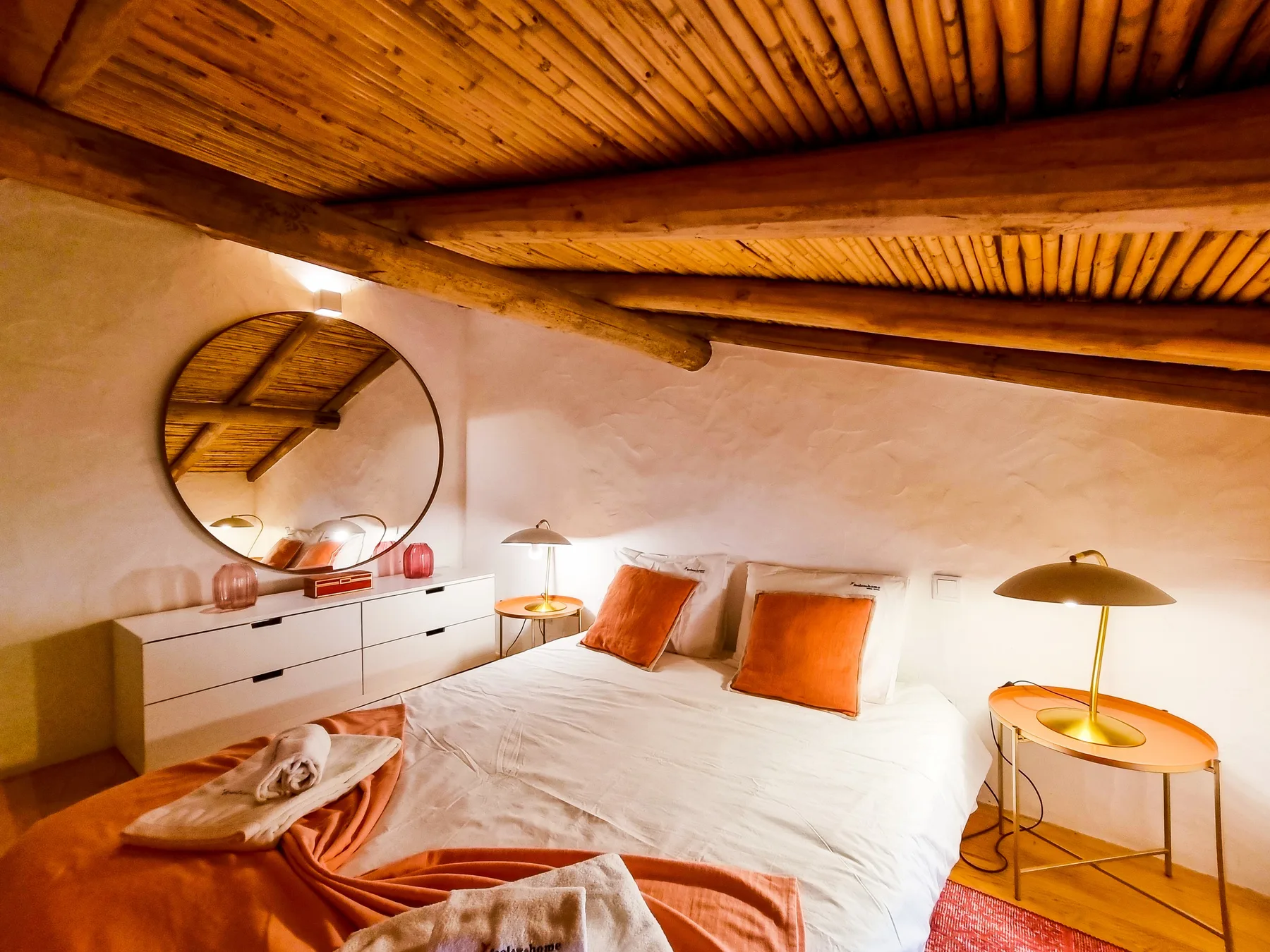 Un dormitorio con una cama, cojines naranjas y un techo de madera.