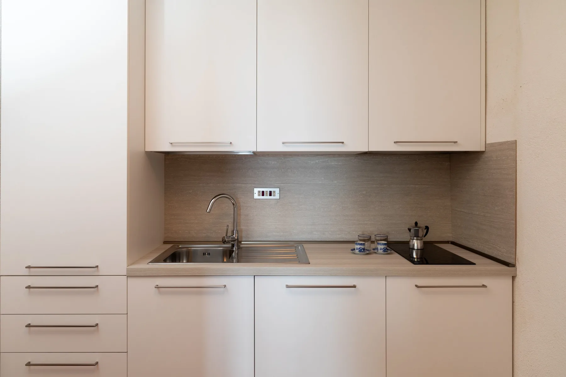 Una cocina compacta con gabinetes blancos, fregadero y una placa de cocción oscura.