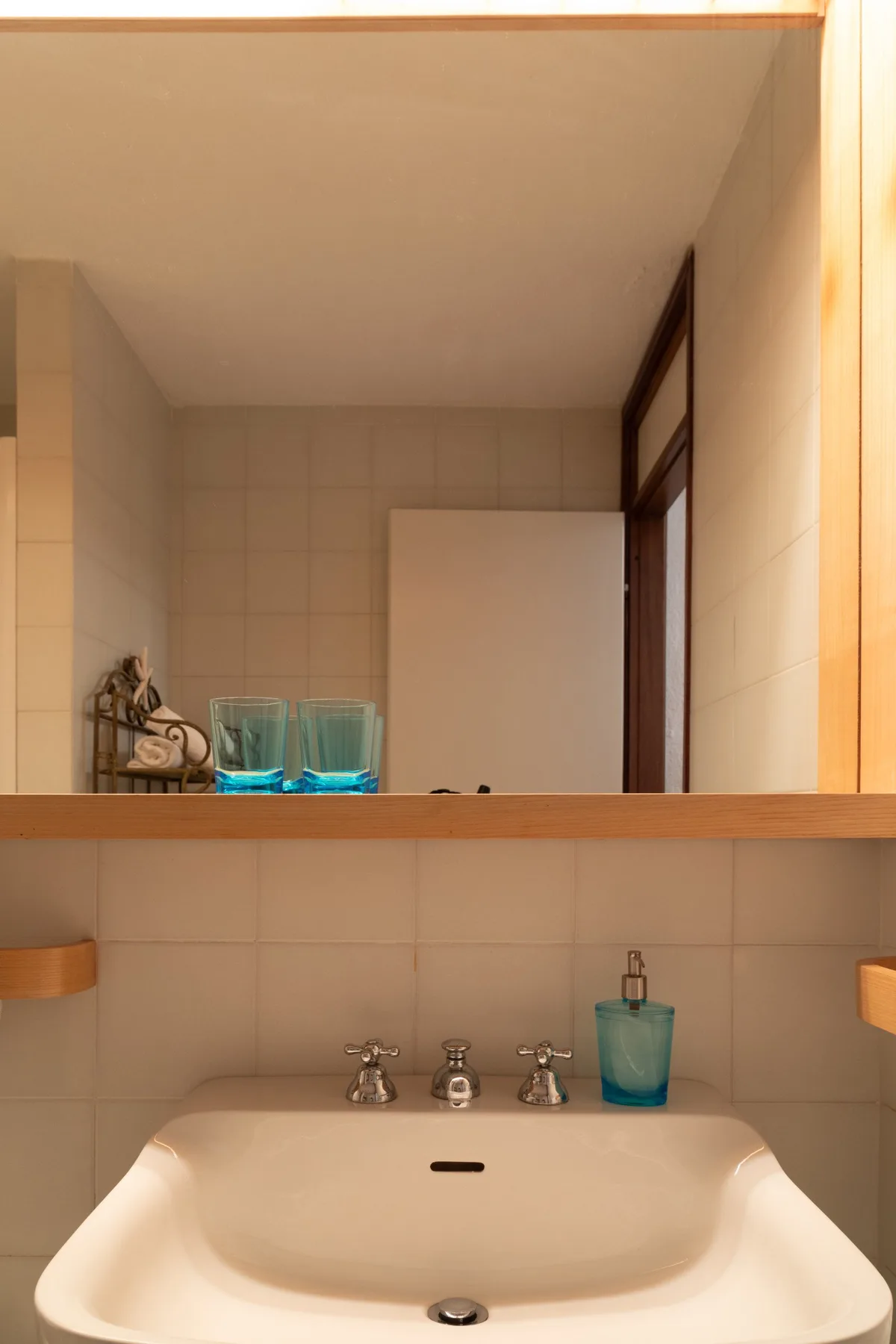 Un lavabo de baño está bajo un espejo amplio, con paredes de azulejos al fondo.