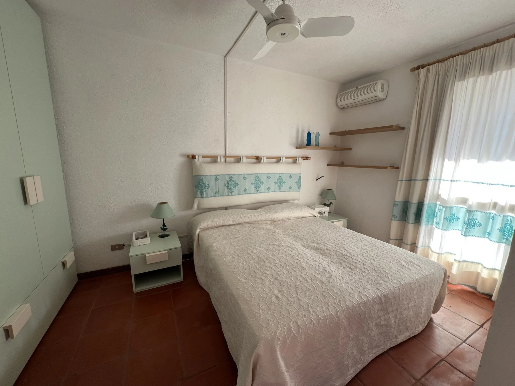 Un dormitorio con cama doble, mesa de noche y cortinas en la ventana.