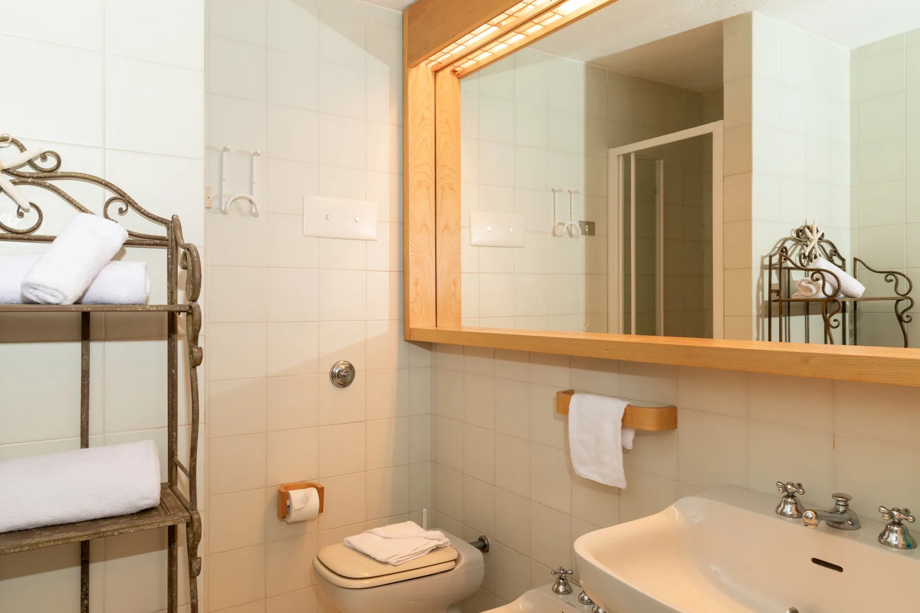Un baño alicatado con lavabo, inodoro y un gran espejo en la pared.
