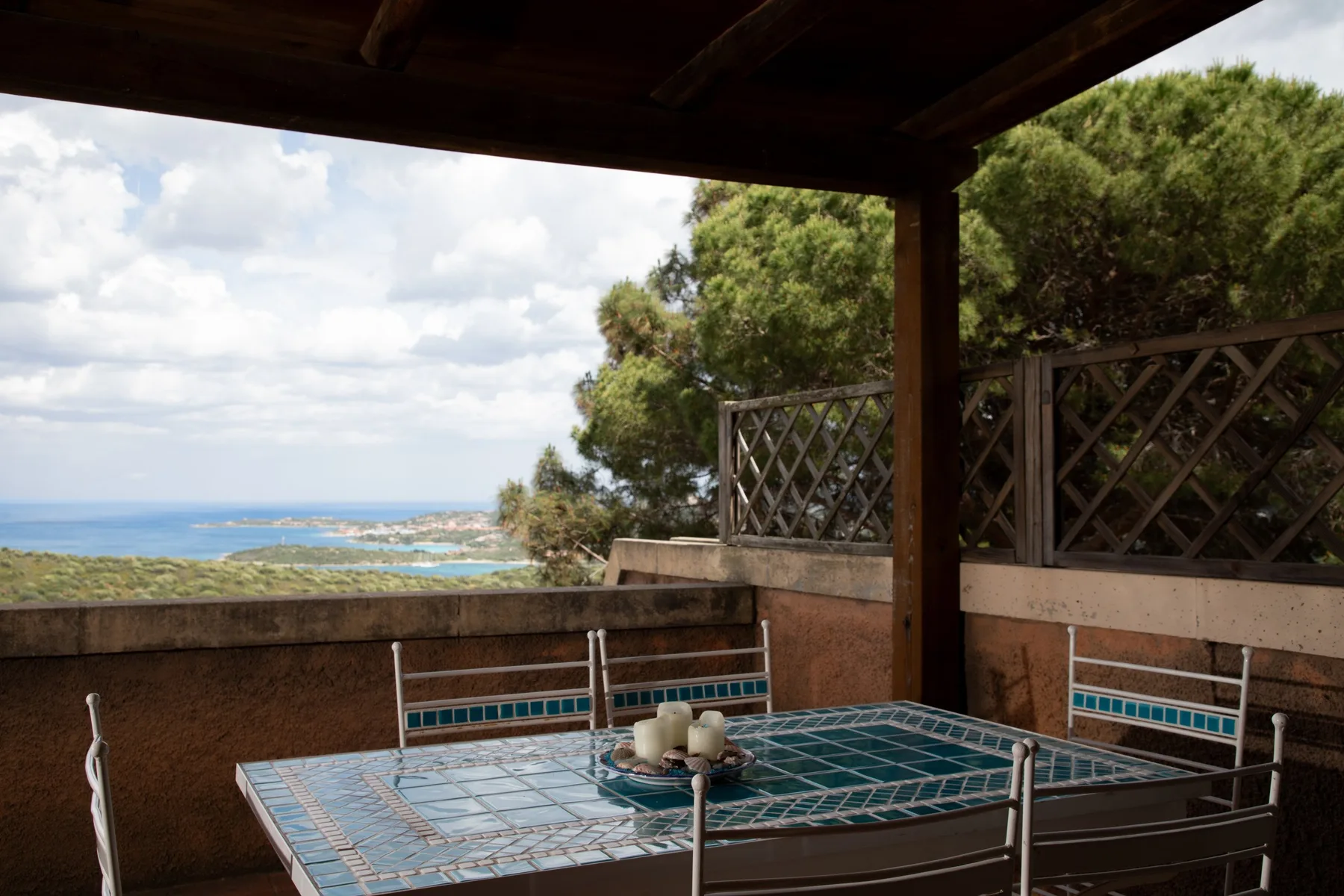 Una zona de comedor exterior cubierta da al mar, con una mesa de azulejos y asientos metálicos.