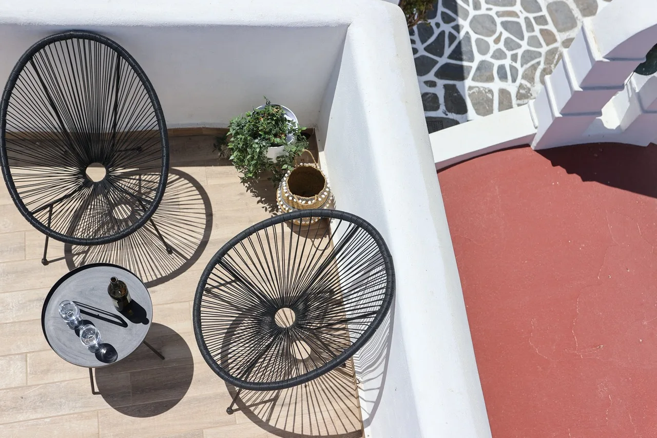 A small outdoor patio has two woven chairs, a round table, and potted plants.