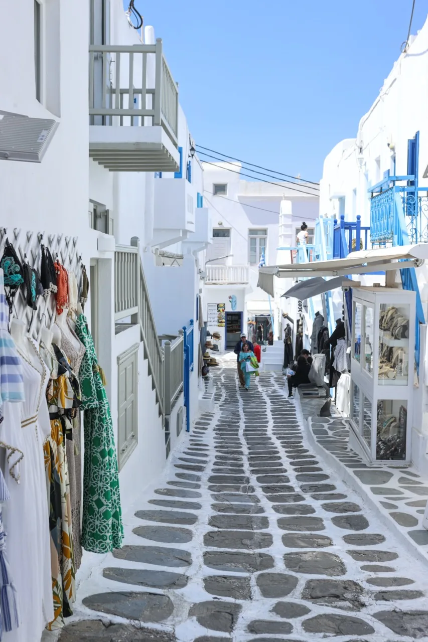 A narrow pedestrian lane lined with white buildings and clothing displays.