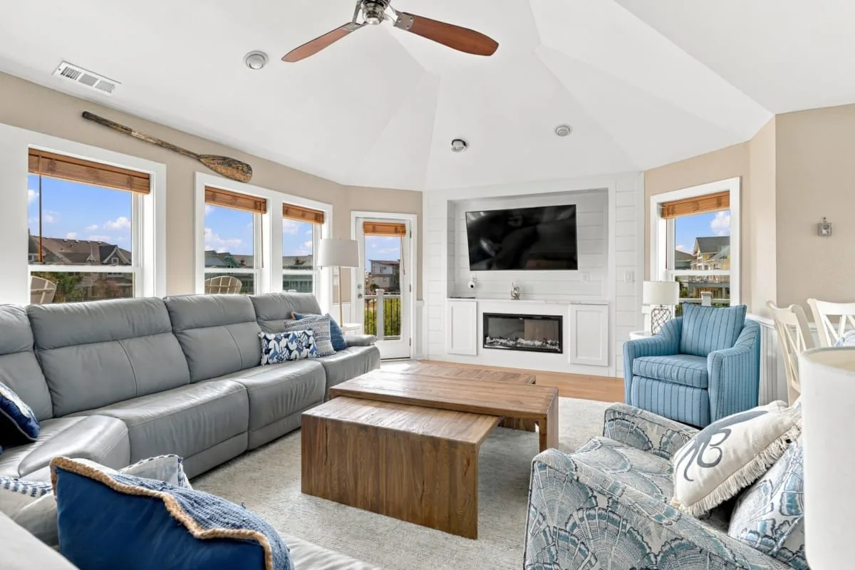 A bright living room with a large seating area and a fireplace beneath a television.