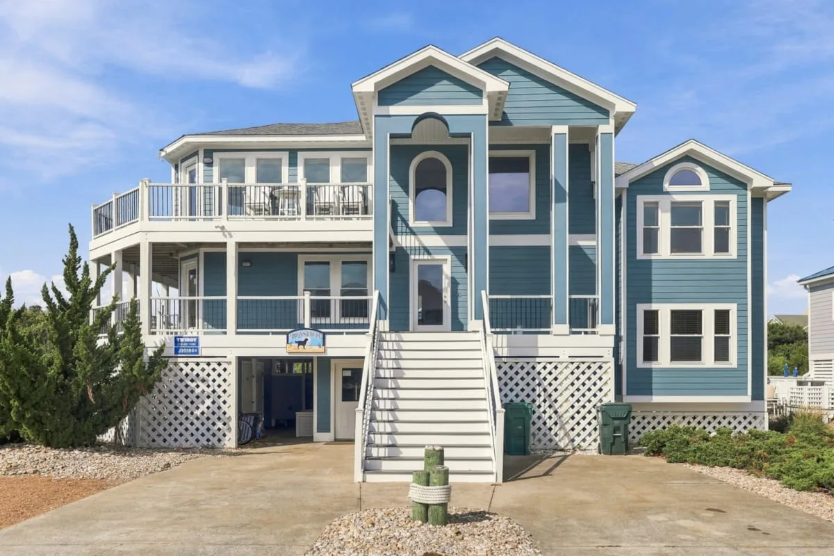 A large blue coastal-style house with white trim and an exterior staircase.