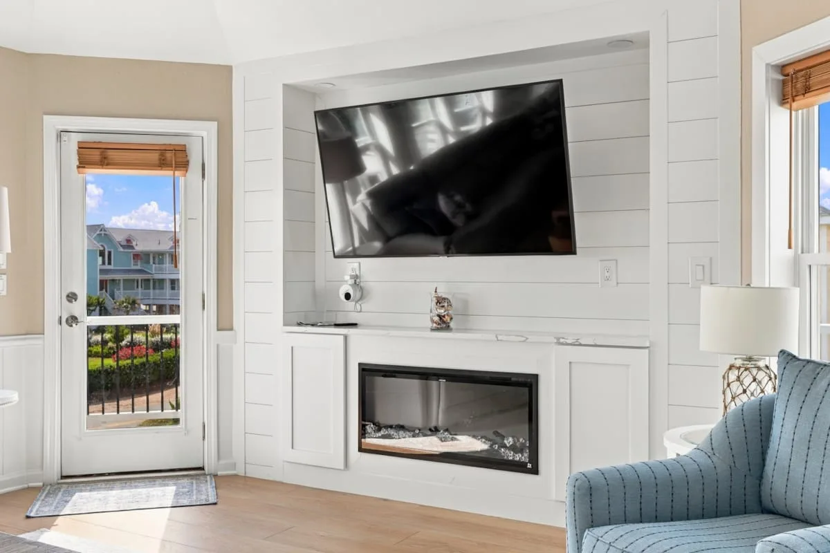 A bright living room with a television above a fireplace and a blue armchair.