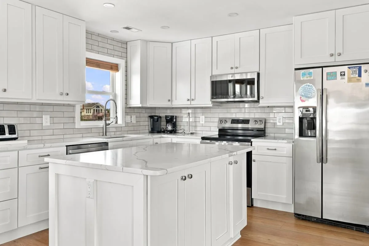 A bright kitchen with white cabinetry, stainless steel appliances, and a central island.