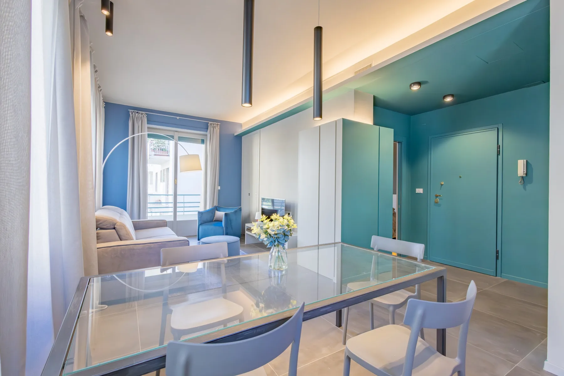 A bright dining area with a glass table and seating beside a living area.