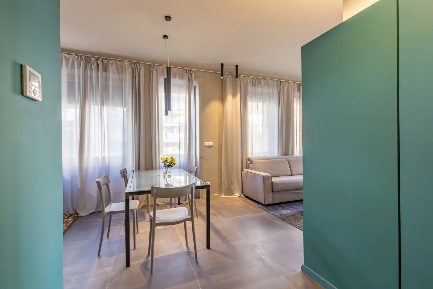 A bright living and dining area with a table, seating, and tall curtained windows.