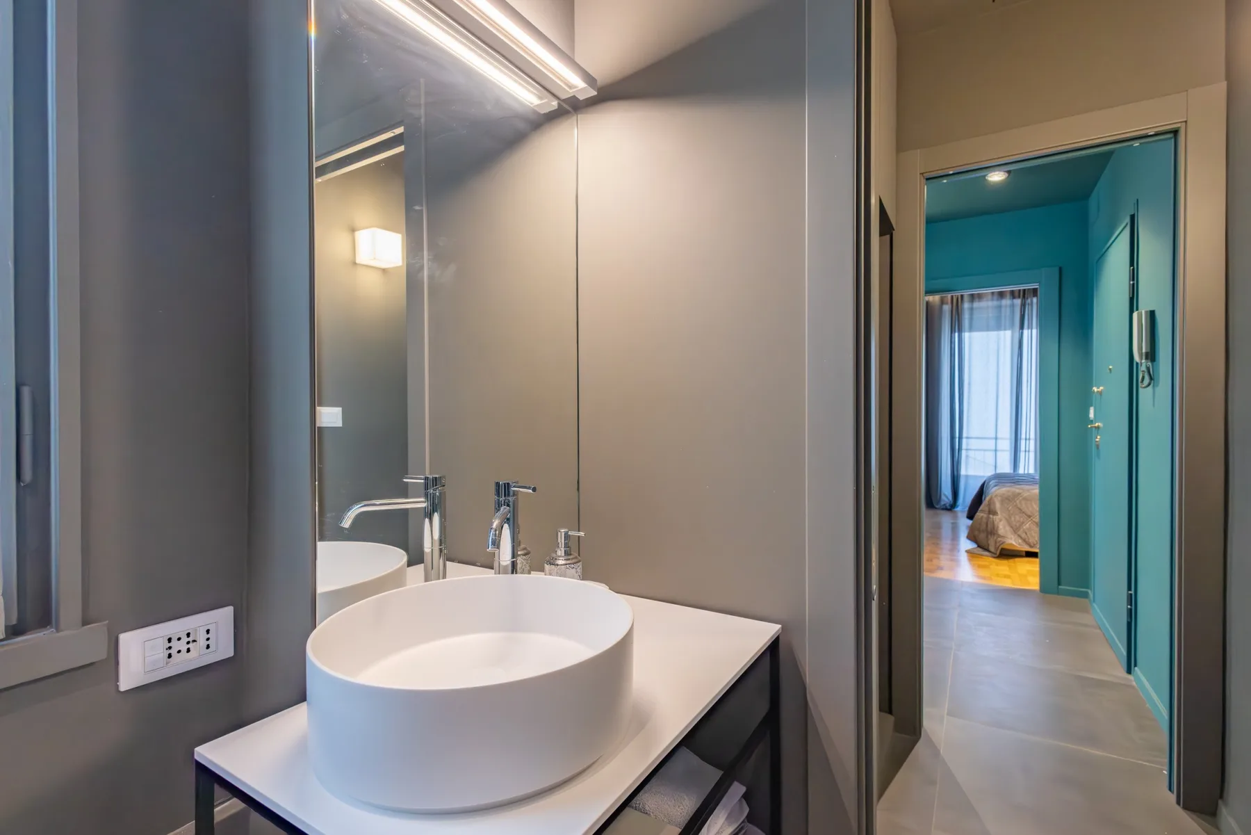 A modern bathroom with a round vessel sink and a view into an adjoining bedroom.